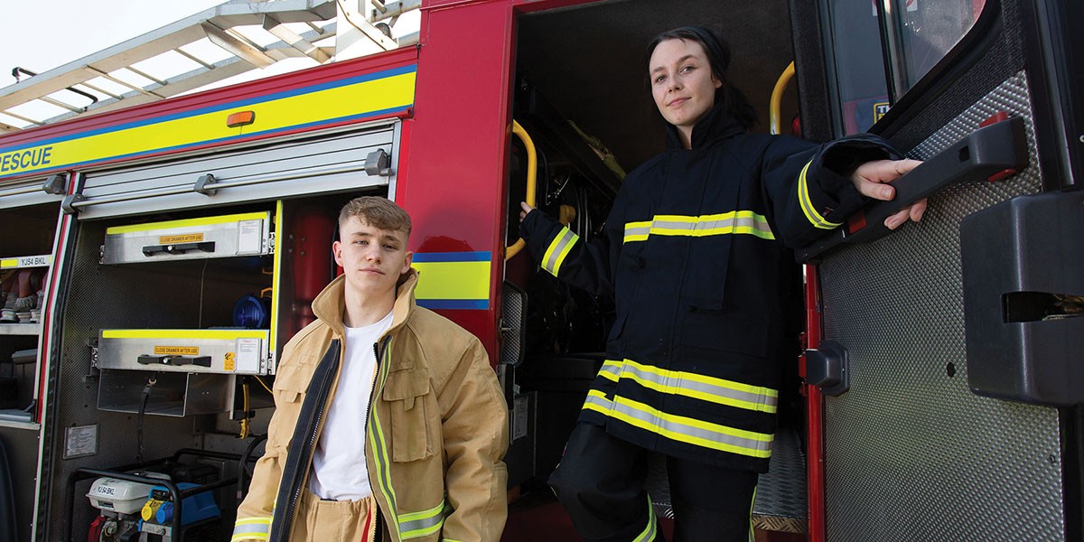 young male and female firefighters standing by engine